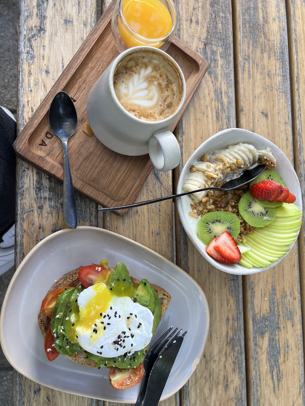 Desayuno de Café Nómada: café con leche, jugo de naranja, tostadas con palta y huevo poché, y bowl de frutas con granola